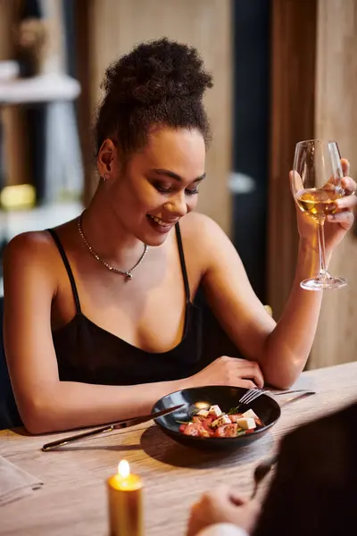 stock image cheerful african american woman holding wine glass next to man during date on Valentines day