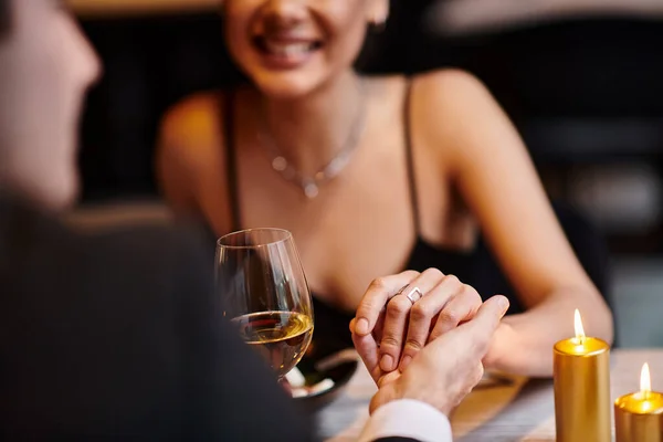 cropped view of man holding hand of happy woman during romantic dinner on Valentines day