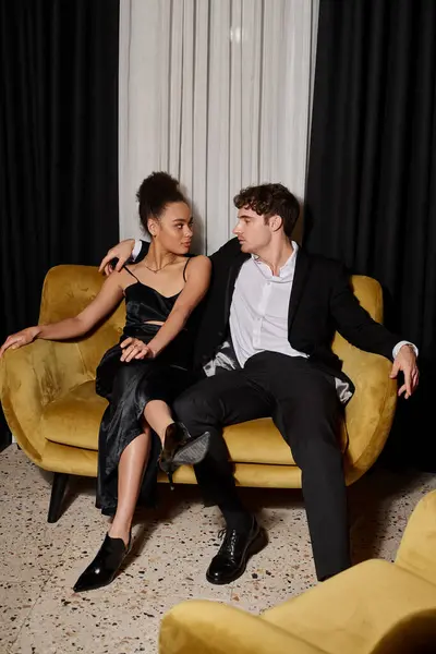 Stock image young african american woman in black dress and handsome man in elegant suit sitting on velvet sofa