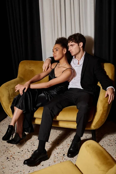 黒いドレスとエレガントなスーツの若いアフリカ系アメリカ人女性が一緒にビロードソファに座って — ストック写真
