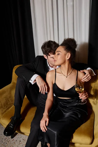 Adam zarif Afro-Amerikan kadınına sarılıyor elinde bir bardak şarap ve kadife koltukta oturuyor.