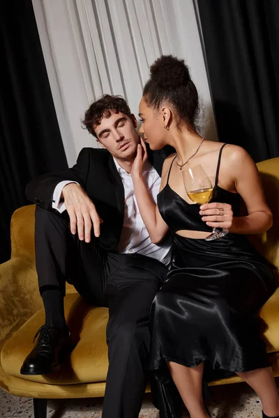 stock image elegant african american woman holding glass of wine and flirting with man in suit on velvet sofa