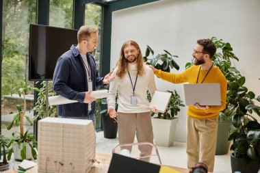 İyi görünümlü neşeli mimarlar günlük giysiler içinde birlikte çalışarak iş birliği yapıyorlar.
