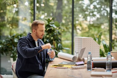 good looking focused man in casual attire working on his startup with his laptop in office clipart