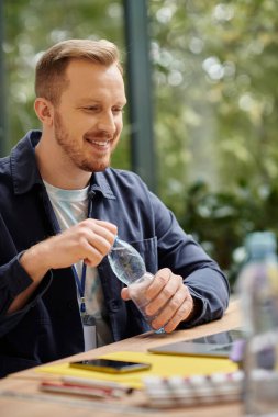 merry handsome man in everyday attire sitting at desk and working on his startup in office clipart