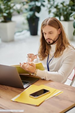 concentrated handsome man in casual attire with long hair working on his startup in office clipart