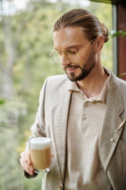 Sakallı ve zarif takım elbiseli çekici bir adam sıcak kahvesini içiyor.