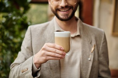Güzel görünümlü, sakallı ve zarif takım elbiseli mutlu bir adam. Sıcak kahvenin tadını çıkarıyor.