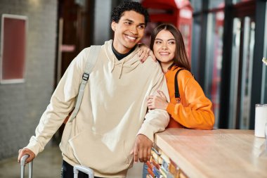 Joyous interracial couple smiling at hostel reception desk, seemingly excited about their journey clipart