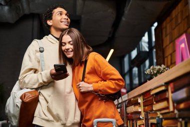 Yurt kütüphanesinde kitaplarla çevrili akıllı telefon ekranına yakından bakan ırklar arası bir çift.