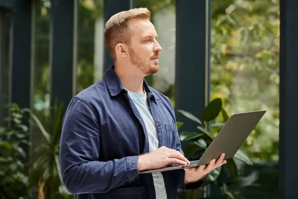 stock image concentrated handsome man in everyday comfy attire holding his laptop while working hard in office