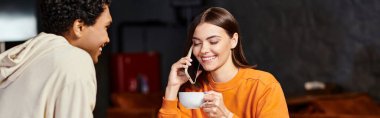 Kafede siyah erkek arkadaşının yanında akıllı telefonuyla sohbet eden mutlu genç bir kadın.