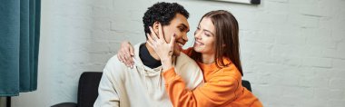 Smiling diverse couple sitting on sofa, woman touching face of black boyfriend, banner clipart