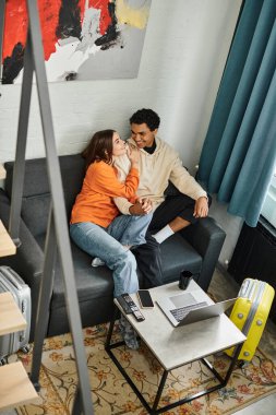 diverse affectionate couple caught in moment of playful conversation on comfy couch, travel concept clipart