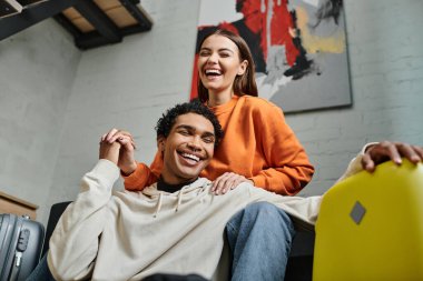 Afro-Amerikan erkek arkadaşıyla el ele tutuşan heyecanlı kadın, yurt odasındaki valizlerin yanında.