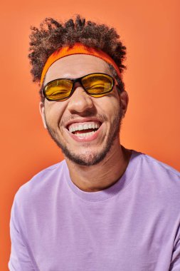 Gözlüklü mutlu Afro-Amerikan adam turuncu arka planda gözleri kapalı, iyimser gülümsüyor.