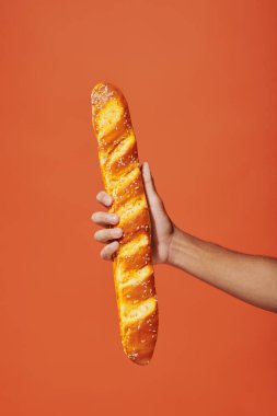 cropped view of person holding freshly baked baguette on orange background, crunchy french bakery clipart