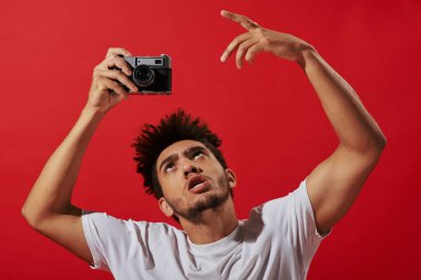 funny and creative african american photographer taking shot on retro camera  on red background clipart