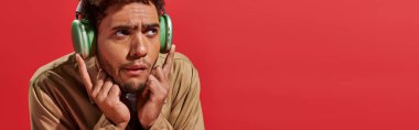 banner of confused african american man in wireless headphones listening music on red background clipart