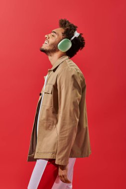 side view of happy african american man in wireless headphones enjoying music on red background clipart