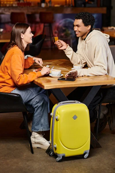 stock image diverse couple having lunch and doing online shopping near their luggage in hostel cafe, credit card