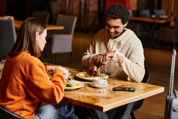 diverse couple shares meal at a restaurant, their faces lit up with joy as they enjoying tasty food