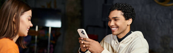 happy black man using smartphone near cheerful girlfriend sits across from him in cafe, banner