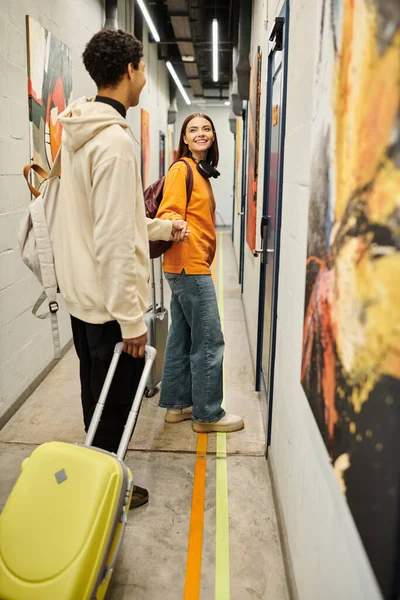 stock image Young multicultural couple smiling and walking with suitcases in a modern hostel hallway