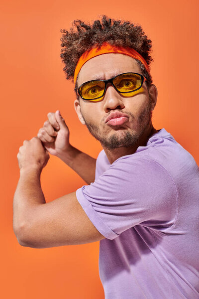 активный молодой африканский американец жестикулирующий и дующийся губами на оранжевом фоне, динамичный