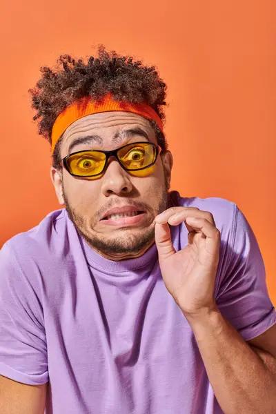 stock image surprised african american man in eyeglasses and headband grimacing on orange background