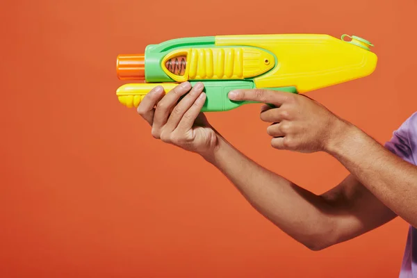 stock image cropped shot of african american man playing water fight with toy gun on orange background