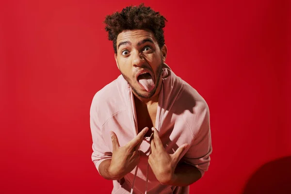 stock image funny african american man pulling pink hoodie and sticking out tongue while on red background