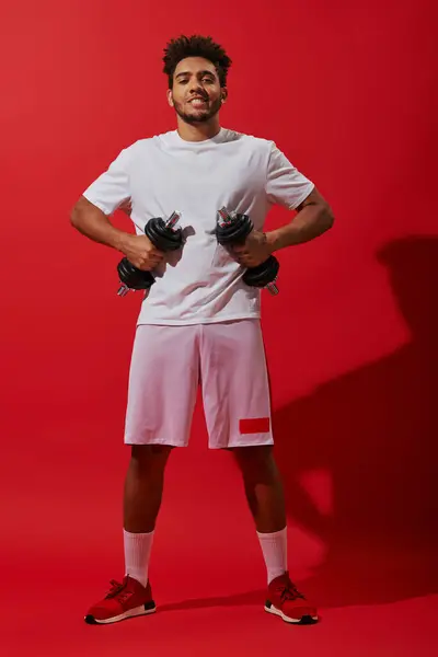 stock image full length of african american sportsman exercising with dumbbells on red background, powerful