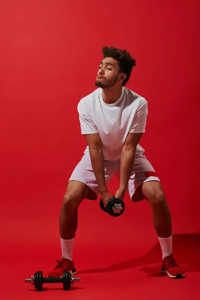 stock image full length of funny african american sportsman exercising with dumbbell on red background