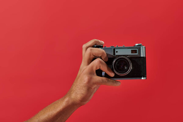 cropped view of african american photographer taking shot on retro camera on red background
