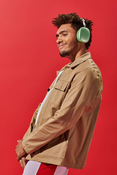 portrait of pleased african american man in wireless headphones enjoying music on red background