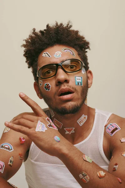 stock image amazed young african american man in sunglasses with trendy stickers on face on grey background