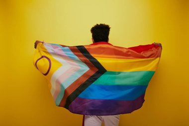 back view of african american man holding rainbow lgbtq flag on yellow background, pride month clipart