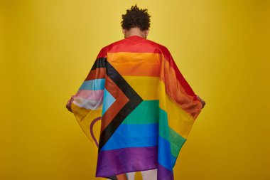 back view of african american man holding rainbow flag on yellow background, pride month clipart