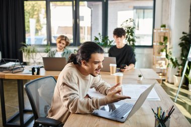 emotional young entrepreneur analyzing data on laptop with colleagues in a modern workspace clipart