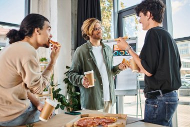 Pizza yiyen ve sohbet eden genç erkekler, arkadaşça ve rahat bir atmosferde, öğle yemeği molasında takım.