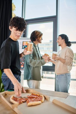 Kahveli kıvırcık takım üyesi dostane ofis atmosferinde pizza yiyor, öğle yemeği molası veriyor.