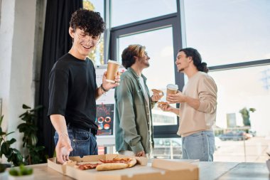 Arkadaşça ofis atmosferinde kahve içip pizza yiyen mutlu takım üyesi, öğle yemeği molası.