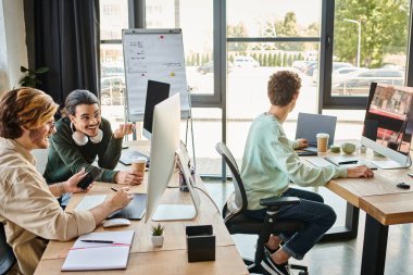 Prodüksiyon ekibi, 20 'li yaşlarda gülümseyen adamların ofisinde rötuş yapmak için cihazların yakınındaki projeyi tartışıyor.
