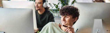 happy curly man engaged in retouching work with stylus pen in hand looking at monitor, banner clipart