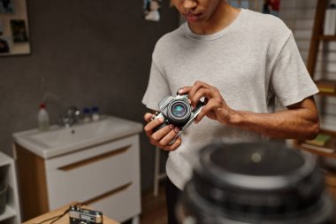 cropped view of young african american photographer expertly handling a vintage camera in photo lab clipart