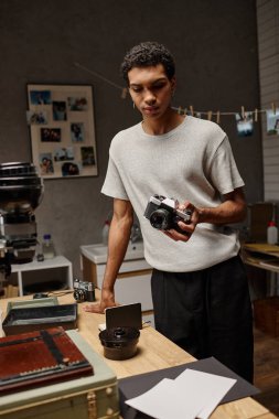 Genç siyahi bir adam fotoğraf laboratuarında film çekerken analog bir kamerayı inceliyor.