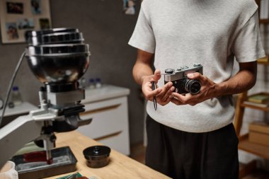 Siyahi adamın, laboratuarda dikilirken elinde analog bir kamera ve kalem tutarken çekilmiş görüntüsü.
