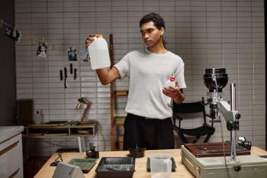 Genç Afrikalı Amerikalı fotoğrafçı karanlık oda, analog film geliştirmede geliştirici çözümünü kontrol ediyor.