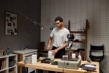 Ciddi genç fotoğrafçı, profesyonel bir karanlık oda ortamında analog film geliştirme işine girmiş.
